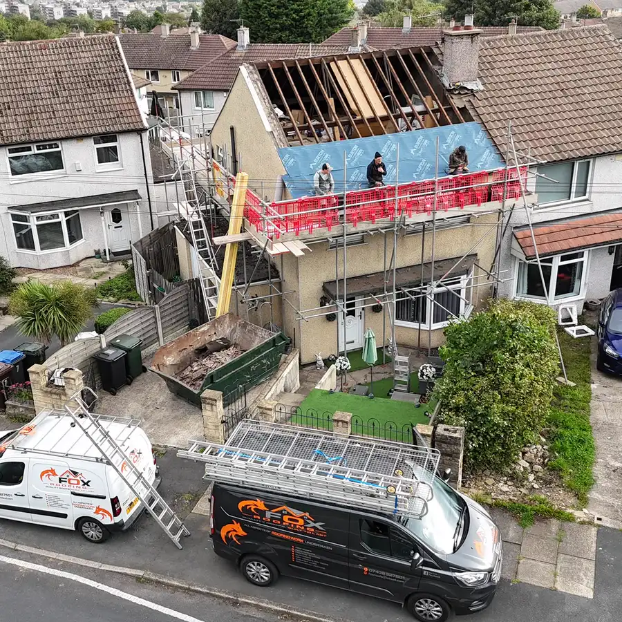Aerial view of a semi-detached roof stripped to the rafters, with the team on the scaffold and both vans outside