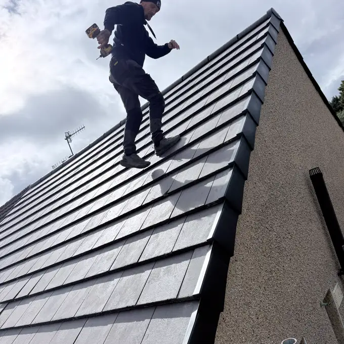 A roofer fixing new grey tiles on a pitched roof with a dry verge along the gable