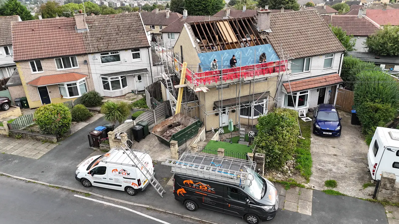 Aerial view of a re-roof under way, with the Fox Roofing vans and a skip outside